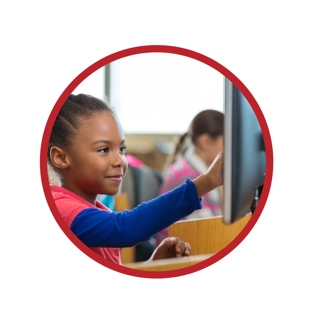 Elementary age African American little girl is smiling while using a desktop computer in public school library or computer lab. Diverse students are wearing casual clothing. Child is pointing at computer monitor screen while working on school assignment.